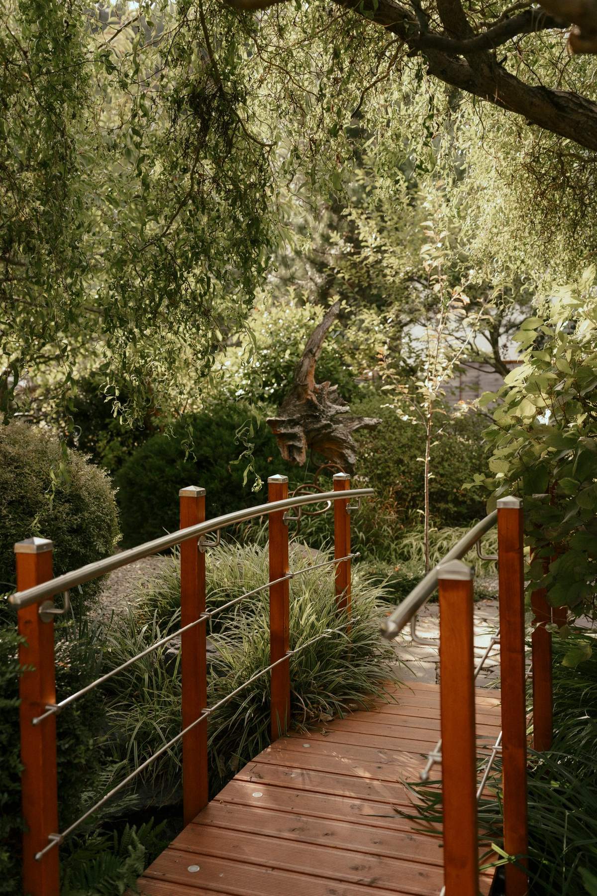 Rote Holzbrücke zwischen Gräsern und Bäumen im Bonsai-Garten