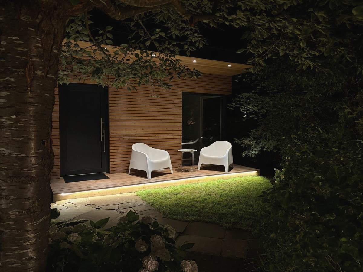 Tinyhouse am Abend mit Licht auf der Terrasse und zwei weißen Sesseln