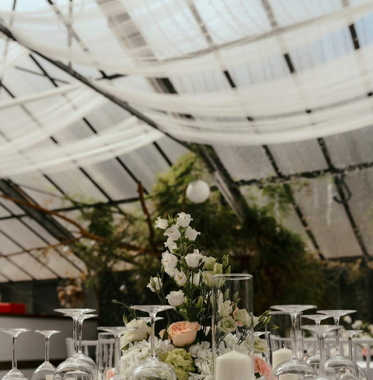 Gedeckter Tisch mit Blumen unter Stoffbahnen und dem Glasdach des Gewächshauses